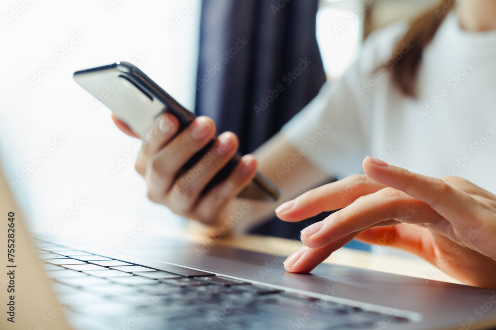 Poster woman using smartphone and hand typing on the computer keyboard in the office.