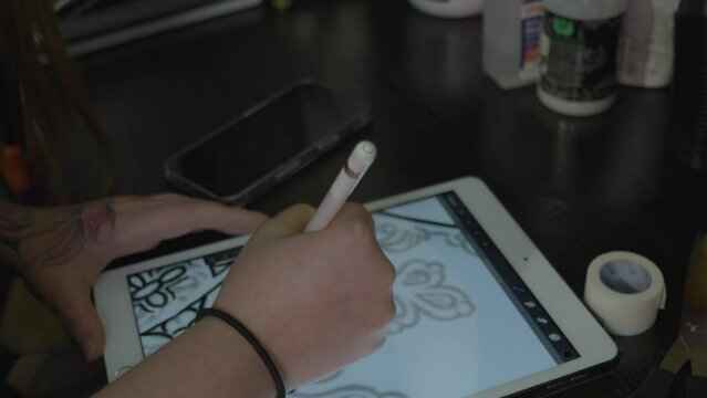 a woman's hand who is a tattoo artist sketches a atttoo design on a tablet to prepare for the tattoo