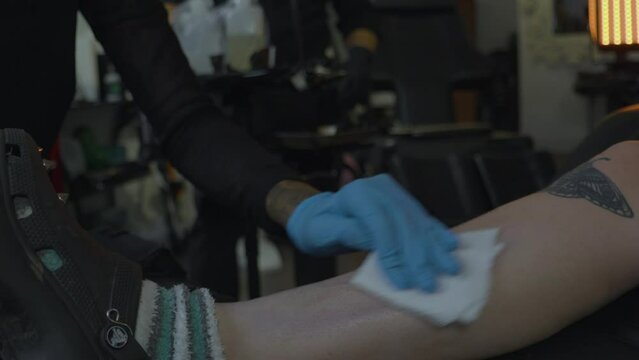 a woman in a tattoo shop sterilizes the leg of a client in preparation of inking a tattoo onto her skin