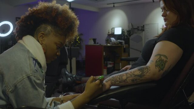 a black female tattoo artist adjusts a light before beginning to draw  a tattoo on her clients hand