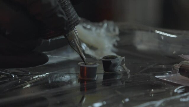 a tattoo artist dips the tip of the tatto pen or iron into ink to load the gun  on a sterile tray for tattooing