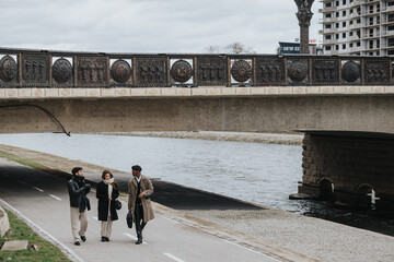 Group of three stylish business associates on a leisurely stroll under a historical bridge,...