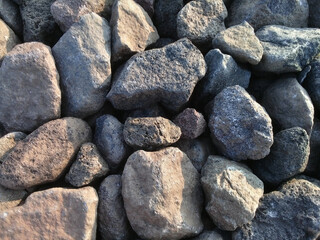 stone wall background, piles of river rocks of various sizes colored dark gray and orange in the sunlight