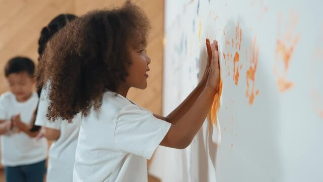 African girl paint the wall with colorful stained hands with friend. Group of multicultural learner standing in front of wall while using hand to create artwork. Creative activity concept. Erudition.