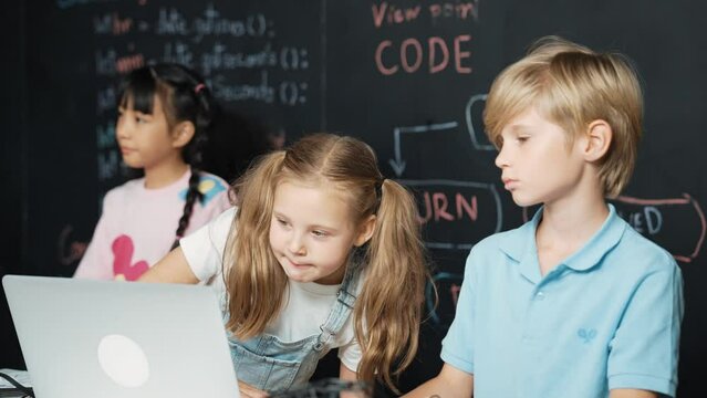 Smart girl using laptop programing engineering code with diverse friends ay table with microchip and main board scatter around in STEM classroom at blackboard written with coding prompt. Erudition.