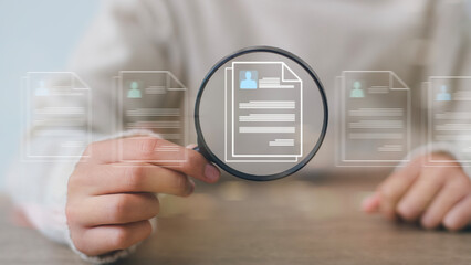 Women holding a magnifying glass with paper. The papers appear to be resumes or job applications. the concept of someone carefully examining these documents. Online recruitment concept