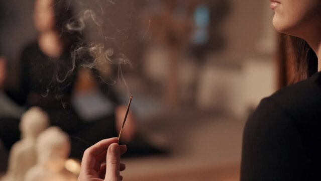 Woman meditating at home. A young attractive female burning an incense stick. Close up.