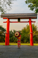 Back view of a young woman wearing a Japanese Yukata and holding a paper umbrella at Torii...