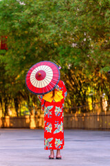 Back view of a young woman wearing a Japanese Yukata and holding a paper umbrella.