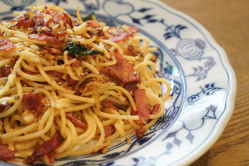 A top view of delicious dried chili garlic bacon pasta served on a vintage plate, placed on a rustic wooden table.