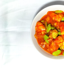 Selective focus. Chili prawns or Sambal Udang with petai or pete in white plate on white background. Indonesia cuisine food. 
