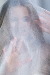 Portrait of a young woman covered with white mesh fabric. A woman hides her face behind a veil cloth.