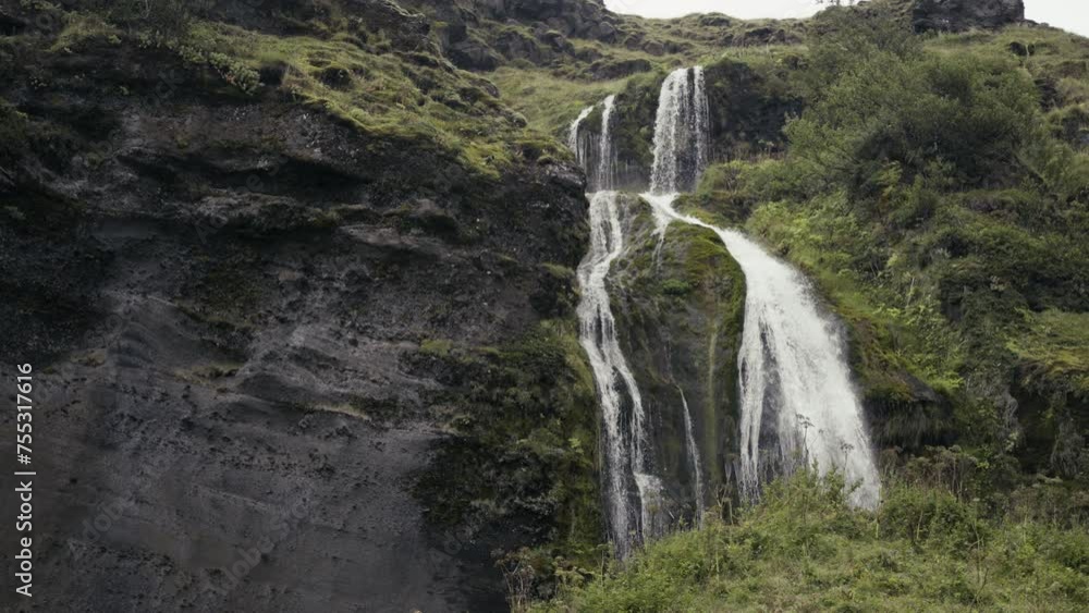 Poster beautiful streams of small waterfall run over a cliff face pock marked with sprigs of grass. shot in