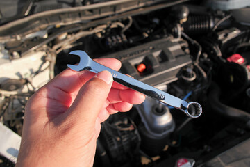 Combination wrench or open end spanner chrome in a car mechanic hand with engine compartment blurred on background, Car repair concept