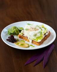 Avocado Egg Toast with Sauce, Garnished with Fresh Herbs and Served with Cucumber Slices and Mustard.
