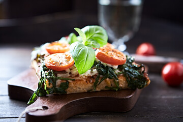 Open-faced toasted cheese sandwich with cherry tomatoes, spinach and fresh basil. Brown wooden background.