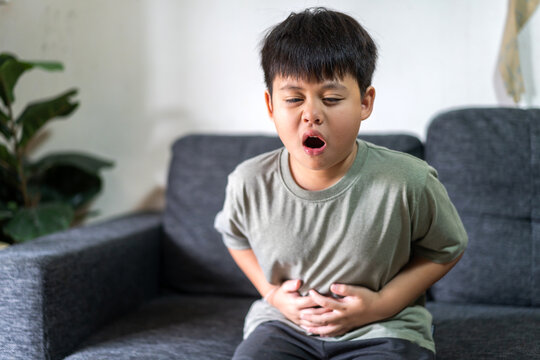 Portrait of sick unhappy little child asian boy touching belly stomach with suffering from stomach ache pain, gastritis, gastroenteritis, food poisoning, diarrhea, intestinal inflammation at home