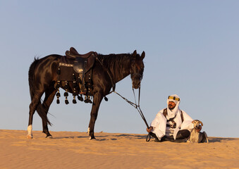 Saudi man in a desert with his horse and dogs