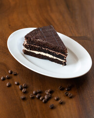 A piece of chocolate cake with white cream, sprinkled with chocolate chips on a plate, decorated with coffee beans.