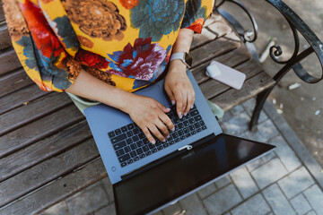 Female hands working on her laptop while sitting on a park. Working outdoors, a woman's hands are typing text on a laptop keyboard, close-up, without a face.