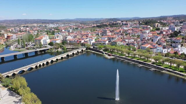 Scenic drone view of small Portuguese city of Mirandela on banks of Tua river with bridges and modern water fountain overlooking terracotta roofs