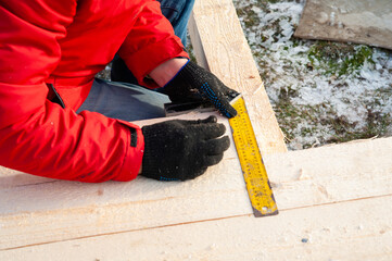 A man in a red jacket is engaged in construction using wooden planks - 755389073