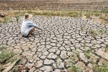 A poor farmer squatting and watching the barren agricultural field. The cause is a lack of water during the long dry season which is caused by the phenomenon of global warming.