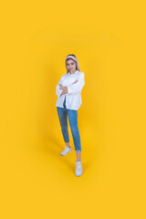 Fototapeta na wymiar Young confident woman, full body portrait of caucasian cool young confident woman stand with folded arms. Smiling, proud, satisfied blonde girl wear causal white shirt and blue jean. Yellow background