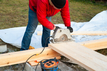 A man in a red jacket is engaged in construction using wooden planks - 755390821