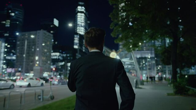 Following shot of a man in suit walking alongside road while returning home during evening time.