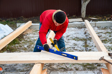 A man in a red jacket is engaged in construction using wooden planks. Measures level - 755391833