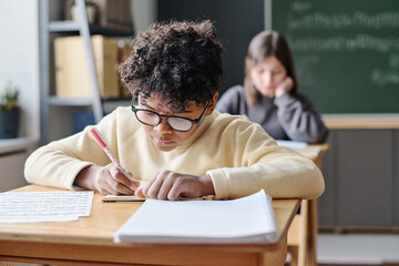 Selective focus shot of African American boy wearing eyeglasses writing in notebook during music...