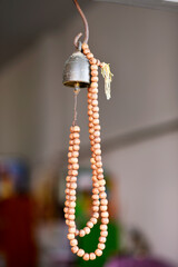 A brown wooden rosary is hung from a golden bronze bell on a blurred background.