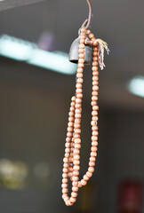 A brown wooden rosary is hung from a golden bronze bell on a blurred background.