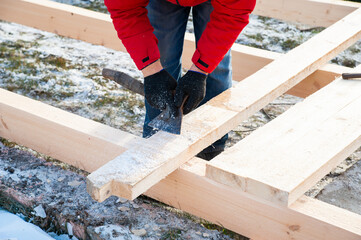 A man in a red jacket is engaged in construction using wooden planks - 755396625