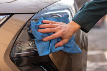 Man is drying up a car after washing it. Closeup man's hand is washing a car. Car washing and cleaning concept.