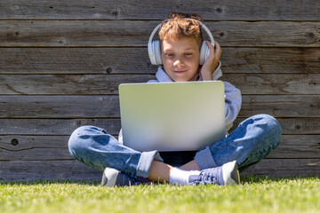 A boy using a laptop and headphones outdoors - 755400699