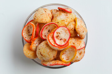 Kerupuk seblak, is colorful round crackers with spicy chili powder topping. In transparent glass bowl, isolated on white background, flat lay or top view