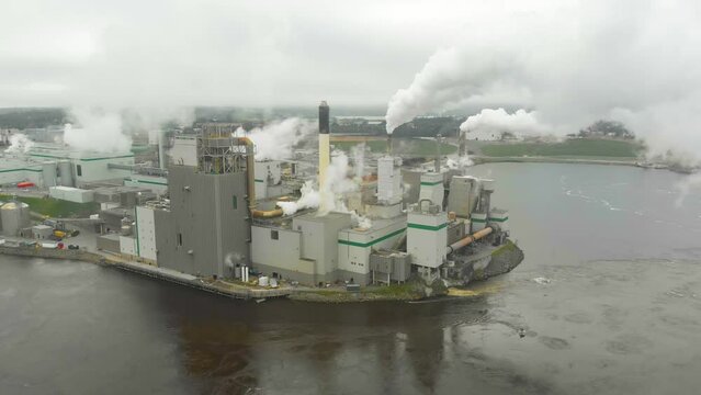 Static aerial shot of the Irving Pulp Factory shooting toxic smoke into the air next to the reversing falls in New Brunswick.