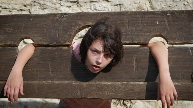 Head in ancient guillotine. A view of child head in guillotine in the city place. A concept of playful mood during medieval festival.