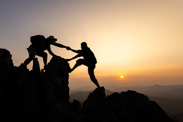 Fototapeta premium silhouette of Teamwork of two men hiker helping each other on top of mountain climbing team. Teamwork friendship hiking help each other trust assistance silhouette in mountains, sunrise.