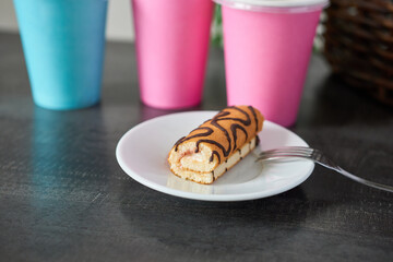 Biscuit roll on a white plate and paper cups on the table. A snack at the café.