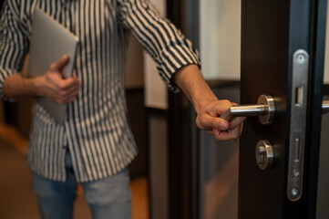 Man in striped shirt with laptop in hands opening door in the hotel