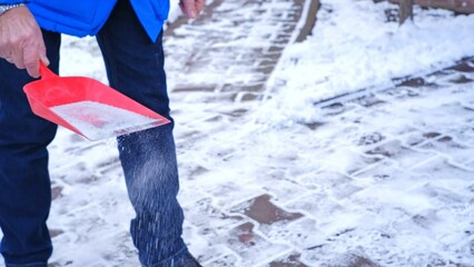 Caucasian Man Sprinkles Salt on House Driveway to Create Brine Solution Melt Snow and Prevent Ice...