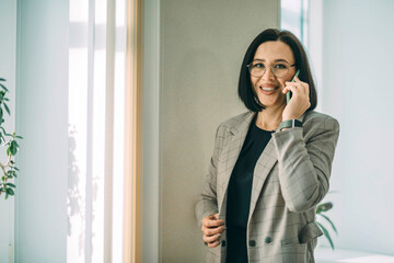 Smiling businesswoman using her phone in the office. Small business entrepreneur talking on mobile phone and smiling while communicating in office