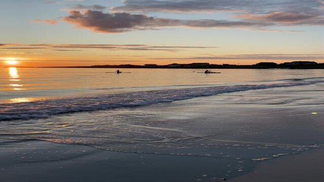 Two persons on kayaks in the midnight sun, Lofoten, Norway, near Ramberg beach. Partly cloudy, orange colours, calm sea. Arctic summer.