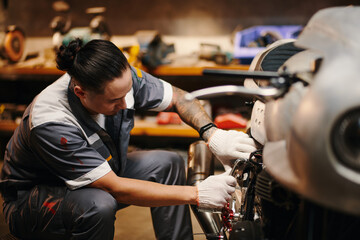 Mechanic in uniform fixing broken motorcycle of client - obrazy, fototapety, plakaty