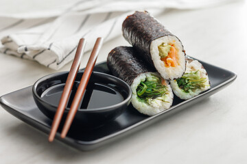 Sushi rolls on Plate with bowl of soy sauce and chopsticks.