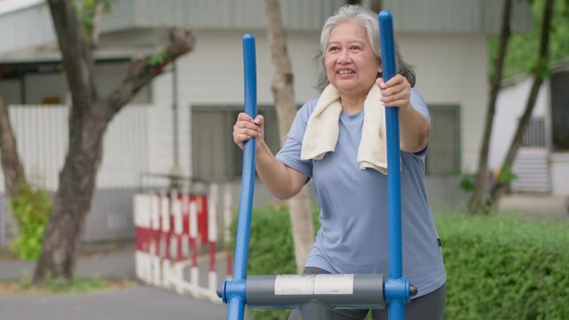 Senior Asian woman in casual workout in exercise stations in public park. Represents keeping young with physical activity, Open air gym. Physical health concept. Outdoor fitness equipment in city park