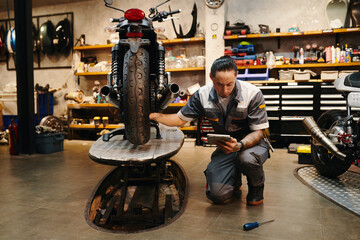 Serious repairman with tablet computer examining motorcycle